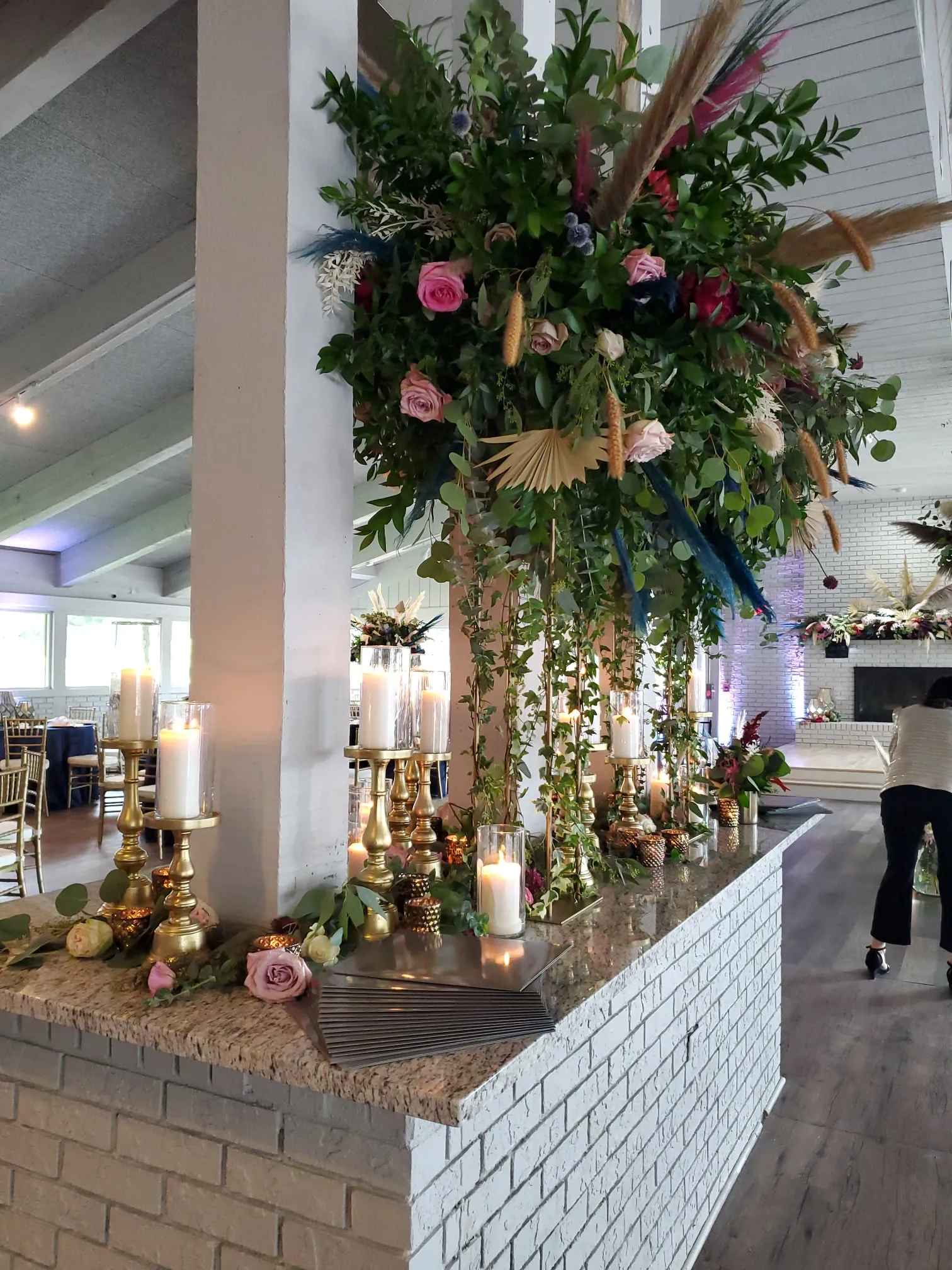 An elaborate floral installation cascading from a column at The Little Cottage, with gold candleholders and pillar candles on the bar below